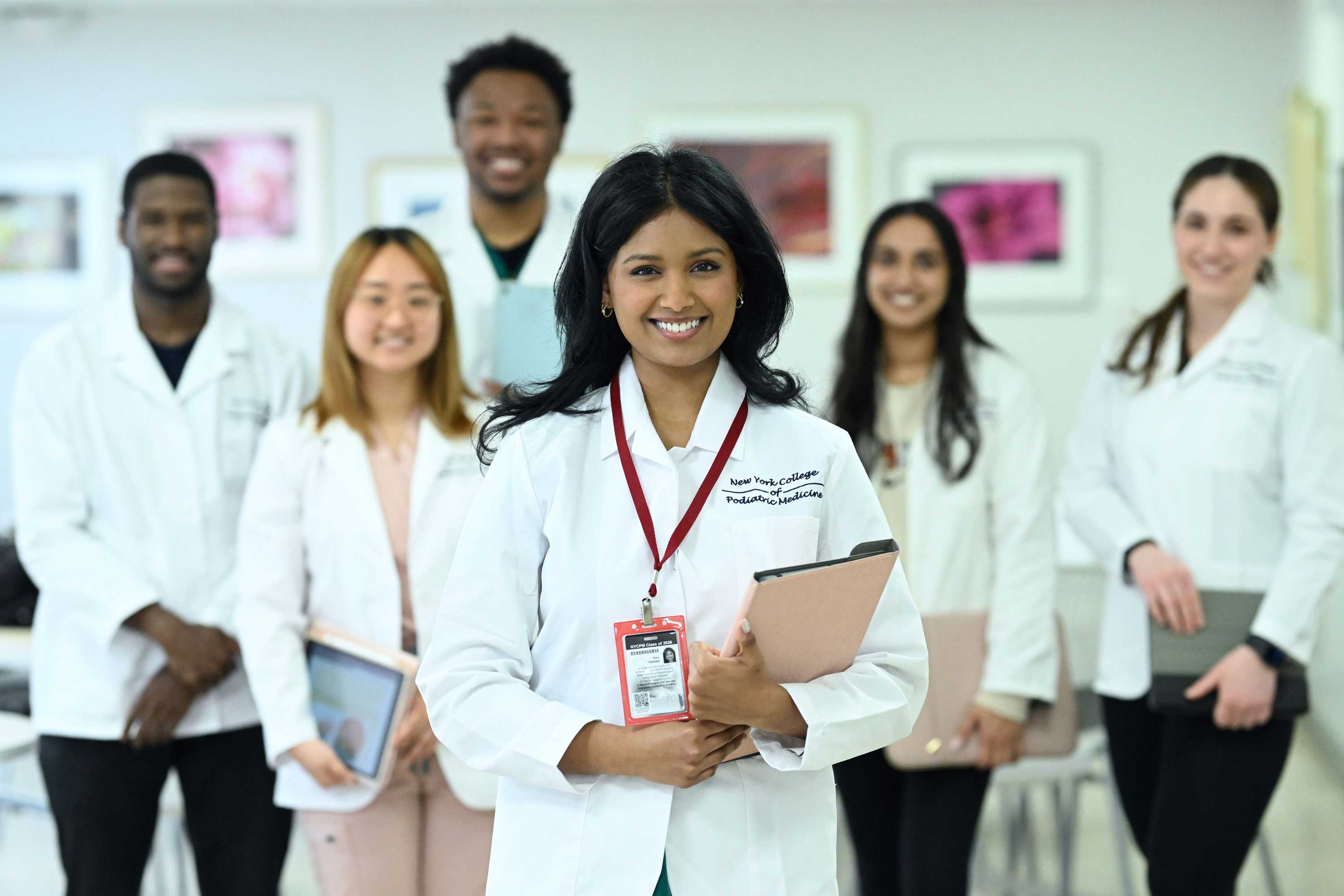 Female NYCPM student smiling and wearing white coat while standing in front of other NYCPM students